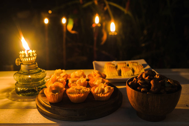 Primo piano di merenda tradizionale durante Hari Raya Aidilfitri in Malesia chiamato crostata kuih o crostata di ananas, anacardi e cornflakes miele con lampada ad olio d'epoca di notte
. - Foto, immagini