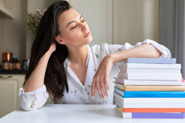 Indoor image of young woman posing at home with her reading stack of books. Smart female student rests on stack of books. Lifestyle, business and education concept - Foto, Bild