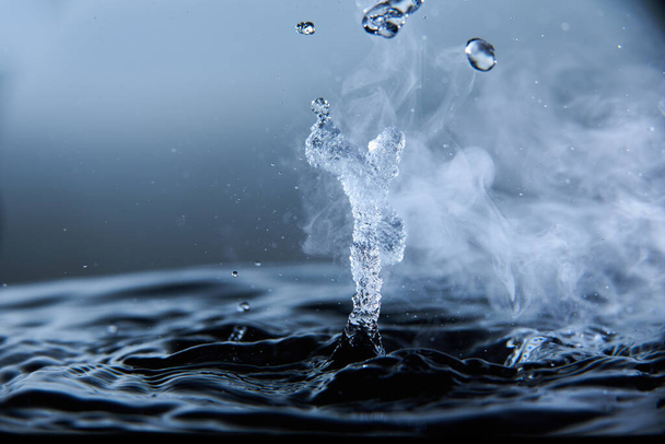 Boiling water splash with steam on dark blue background closeup. - Fotó, kép