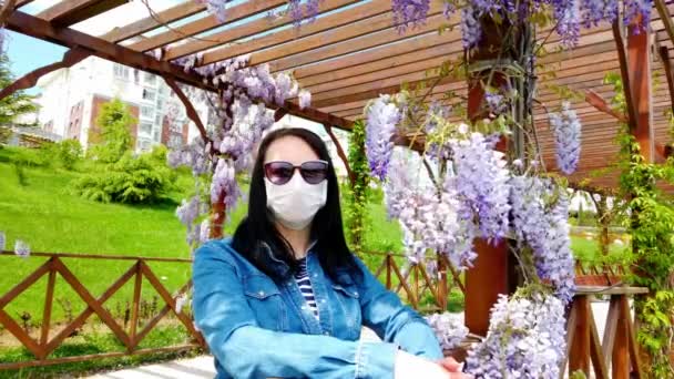 Brunetka dziewczyna w masce medycznej na tle kwitnącej magnolii. - Materiał filmowy, wideo