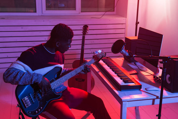 Create music and a recording studio concept - African american man guitarist recording electric bass guitar track in home studio - Фото, зображення