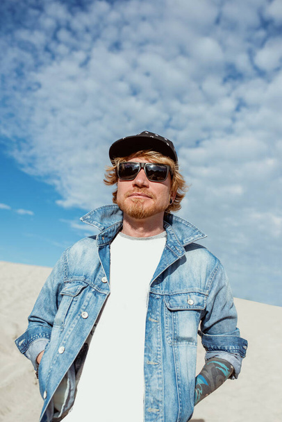 portrait of stylish man in jeans clothes and hat in sunglasses in the desert. Male, style, fashion, nature concept - Photo, Image