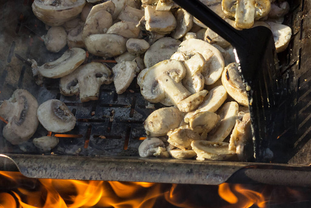 juicy appetising champignons are cooking on grill or BBQ steam. The cook mixes the mushrooms with a kitchen spatula. Selective focus. Food background. Delicious healthy meals for vegetarians. - Photo, Image