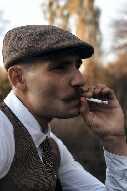 Ретро 1920-х годов портрет английского гангстера с плоской кепкой. Курит сигарету на улице
.. - Фото, изображение