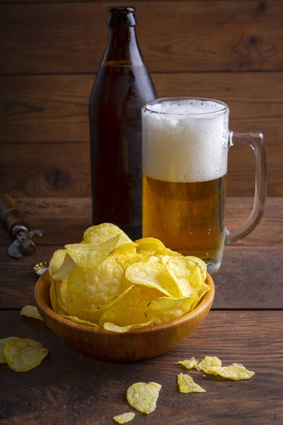 Glass of beer, potato chips in a bowl on a dark wooden background. - Photo, Image