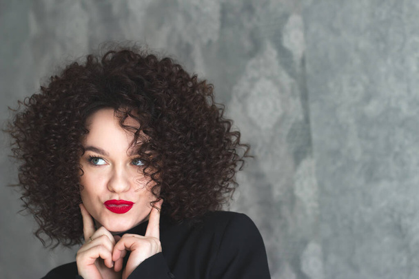 Close-up portrait of a young beautiful girl who is posing. Make-up with red lipstick on the lips. Curly hair of the model. Looking off to the side - Valokuva, kuva