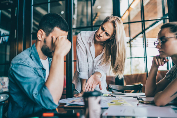 Competent female manager pointing with open palm at fault in report during work meeting while man doing facepalm and his female colleague looking judgemental - Foto, imagen
