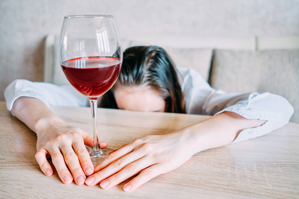 Dívka položí čelo na stůl a v ruce drží sklenici vína. Zavřít. - Fotografie, Obrázek
