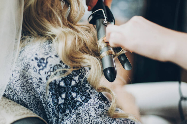 Lockenwickler. Friseur Curling blonde Haare mit professioneller Ausstattung Nahaufnahme, morgendliche Vorbereitungen für den Hochzeitstag. Braut im Friseursalon stylt ihre Haare - Foto, Bild