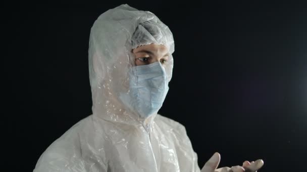 Dokter in een medisch masker en beschermend pak applaudisseert in rubberen handschoenen op een donkere achtergrond. Ondersteuning van artsen in de strijd tegen de coronaviruspandemie. - Video