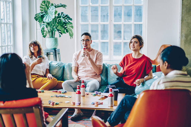 Multiethnic male and female colleagues in casual clothing sitting at table with beverages drinking and chilling out together at stylish living room  - Fotoğraf, Görsel