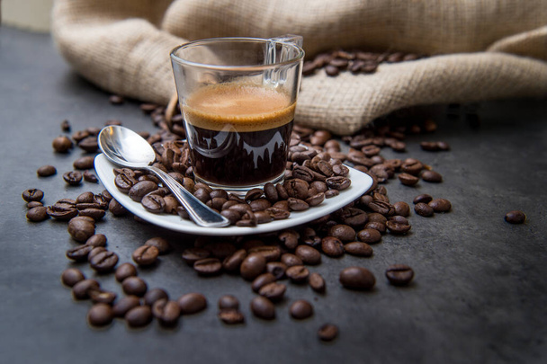 espresso koffie in een glazen beker op een zwarte vloer met koffiebonen snijden licht - Foto, afbeelding