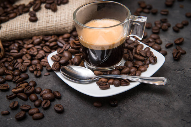 コーヒー豆が光をカットする黒い床の上のガラスカップにエスプレッソコーヒー - 写真・画像