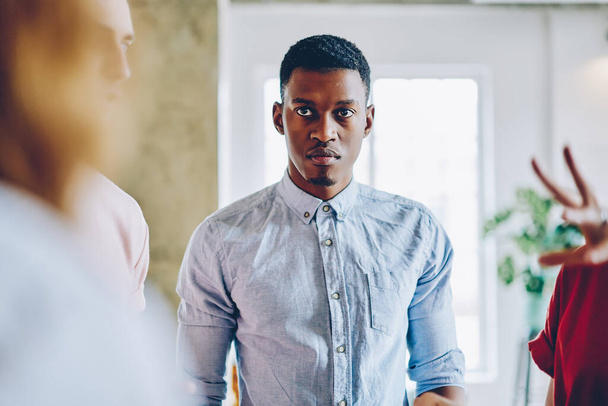 Serious tense African American man in classical shirt angrily looking at speaker on meeting with colleagues in light spacious room - Foto, Imagem