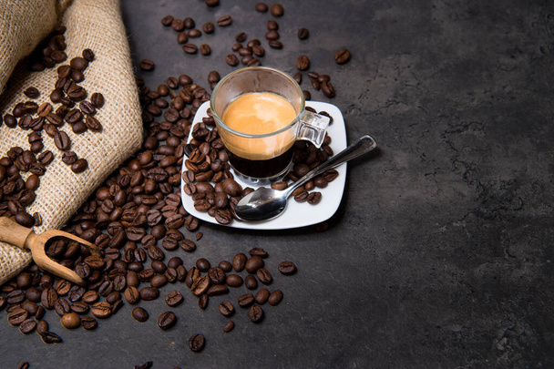 Italian espresso coffee in a glass cup on a black floor with coffee beans cutting light view from top and copy space - Photo, Image