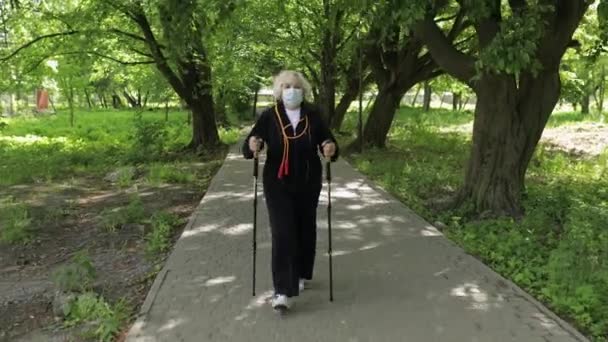 Aktivní starší žena v masce školení Nordic walking v parku v karanténě - Záběry, video