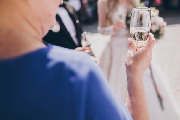 Mujer mayor sosteniendo copa de champán, brindando en la recepción de la boda al aire libre. Madre pronunciando brindis por una nueva feliz pareja de novios. Invitados animando con gafas
 - Foto, imagen