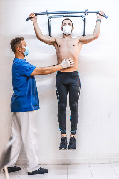 A shirtless patient with a physiotherapist performing a pull-up. Physiotherapy with protective measures for the Coronavirus pandemic, COVID-19. Osteopathy, therapeutic chiromassage - Photo, image