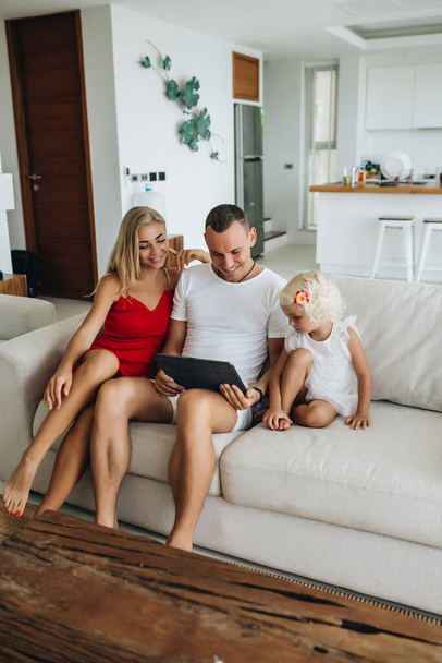 Ευτυχισμένη οικογένεια που χρησιμοποιεί tablet κάθεται στον καναπέ στο σπίτι τους - Φωτογραφία, εικόνα