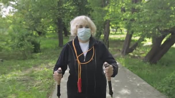 Aktivní starší žena v masce školení Nordic walking v parku v karanténě - Záběry, video