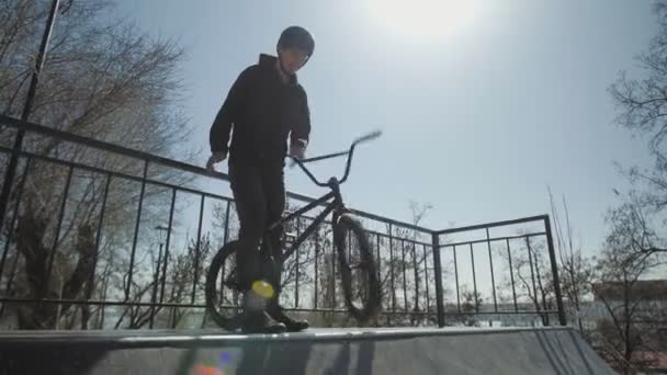 Młody kierowca bmx stojący na szczycie rampy i obracający się do przodu koło w ekstremalnym parku - Materiał filmowy, wideo