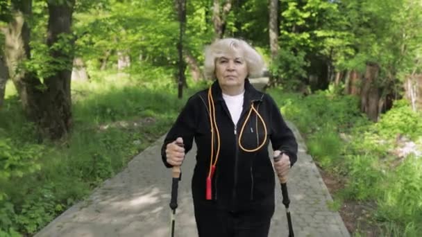 Активна старша жінка навчає скандинавську ходьбу з мисливцями на лижах у парку. - Кадри, відео