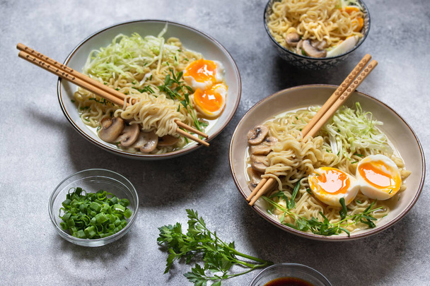 Asian ramen noodle soup with mushrooms, cabbage, green onions and egg. Japanese street food. Gray background, close-up, copy space - Foto, Bild