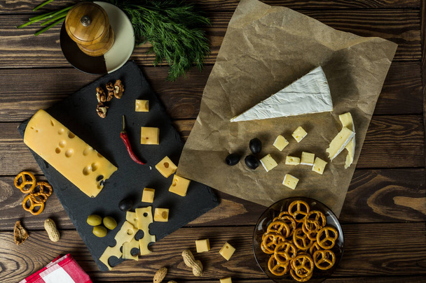Brie cheese Maasdamer cheese. diced cheese on a cheese platter, nuts, herbs, olives, snacks on an old black wooden table. Food for wine and romance, cheese delicacies. Menu design. napkin with a scottish pattern - Fotoğraf, Görsel