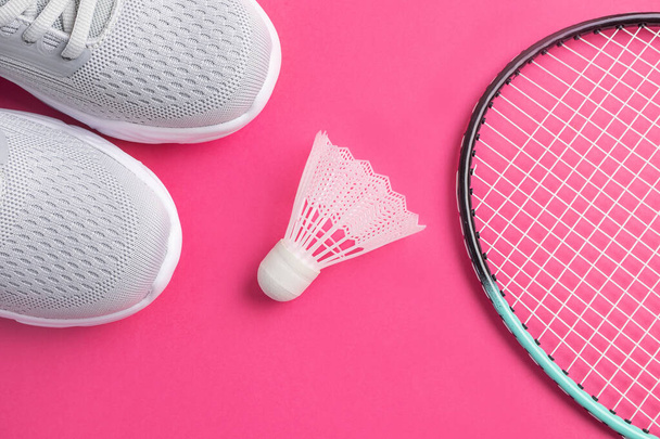 Turnschuhe, Badmintonschläger und Federball auf leuchtend rosa Hintergrund. Das Konzept der Ausrüstung für den Amateursport. Minimalismus. - Foto, Bild