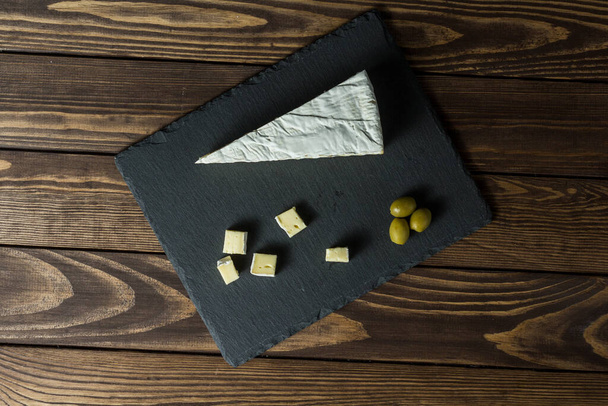Camembert Käse. Käsegericht mit Oliven auf einem alten schwarzen Holztisch. Brie Käse. Essen für Wein und Romantik, Käsespezialitäten. Menüdesign horizontal. Blick von oben. - Foto, Bild