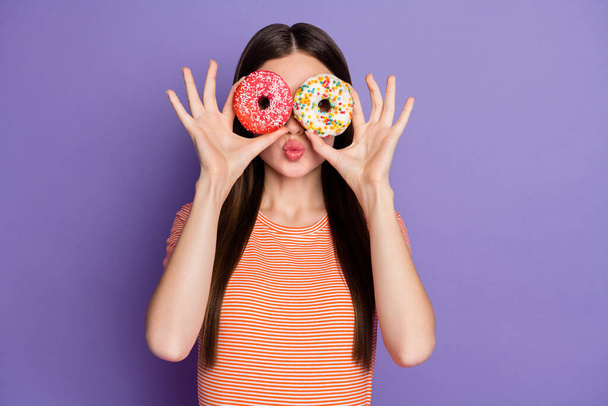Photo of attractive crazy lady long straight hairstyle hold hands glazed doughnuts hiding eyes send air kisses wear casual orange striped t-shirt isolated pastel purple color background - Foto, Imagem