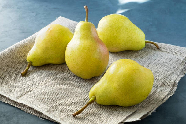 A few fresh pears lie on a simple coarse rustic napkin on a dark blue background. Healthy eating. Horizontal orientation, selective focus.  - Photo, Image
