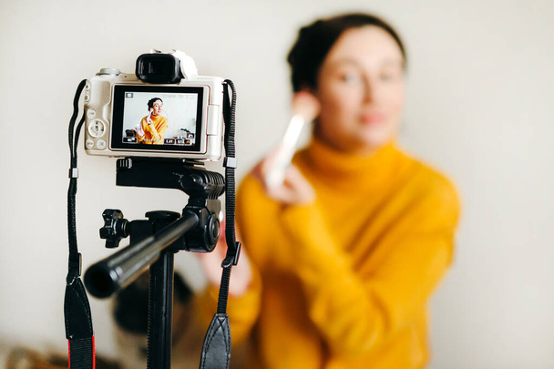 若いブルネットの女の子の美しさのブロガーは、カメラでアイシャドウとブラシを使用する方法を示しています。ブログを撮るというコンセプト。美容・スキンケア. - 写真・画像