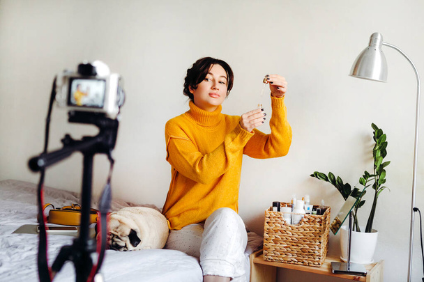 Młoda brunetka blogerka piękna pokazuje, jak serum do pielęgnacji skóry przed kamerą. Koncepcja kręcenia bloga. Piękno i pielęgnacja skóry. - Zdjęcie, obraz