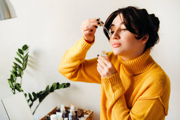 Young brunette girl beauty blogger is showing how to serum for skin care on camera. Concept of filming a blog. Beauty and skin care. - 写真・画像