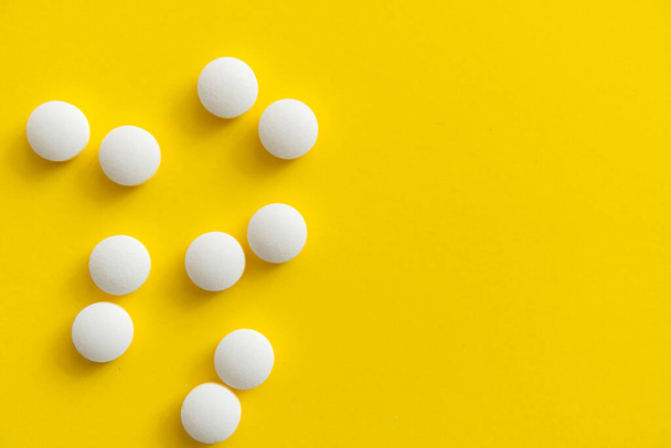 White pills on yellow background. Medicine, medication, painkillers, tablet, medicaments, drugs, antibiotic, vitamin, treatment. Pharmacy theme. Top view on the pills scattered on the white surface. - 写真・画像