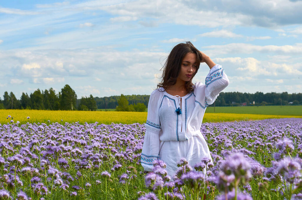 ein junges Mädchen in einem weißen Kleid in einem Blumenfeld. Sommerfelder mit Blumen auf dem Feld - Foto, Bild