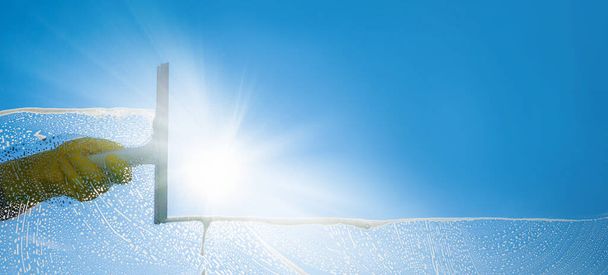 Nettoyant pour vitres avec raclette et essuie-glace par une journée ensoleillée avec un ciel bleu vif. - Photo, image