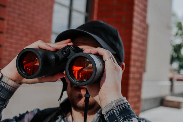 un hombre barbudo mira a través de los prismáticos en la ciudad
 - Foto, Imagen