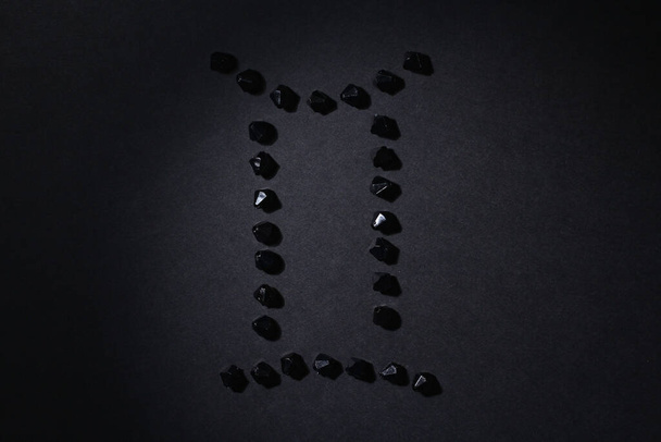 Symbol des Tierkreiszeichens Zwillinge aus schwarzen Steinen auf schwarzem Hintergrund. Niedrige Dunkelziffer. Vignettenbeleuchtung. Horoskop-Thema - Foto, Bild