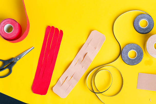 Special physio tapes rolling of different colors and scissors for cutting on a yellow background. Kinesiology taping treatment. - Foto, imagen