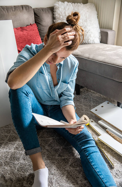 Concentrated young woman reading the instructions to assemble furniture at home in the living roo - Foto, Bild