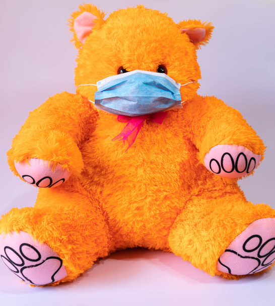 Προστατευτική μάσκα προσώπου φορώντας πορτοκαλί αρκουδάκι παιχνίδι - Φωτογραφία, εικόνα