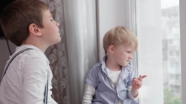 Μικρά χαριτωμένα παιδιά συζητούν μεταξύ τους κοιτάζοντας έξω από το παράθυρο απολαμβάνοντας ξεκούραση στο δωμάτιο - Πλάνα, βίντεο