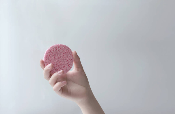 female hand holding a cosmetic sponge for face cleaning and care. pink round sponge in groomed woman's hand - Foto, Imagen