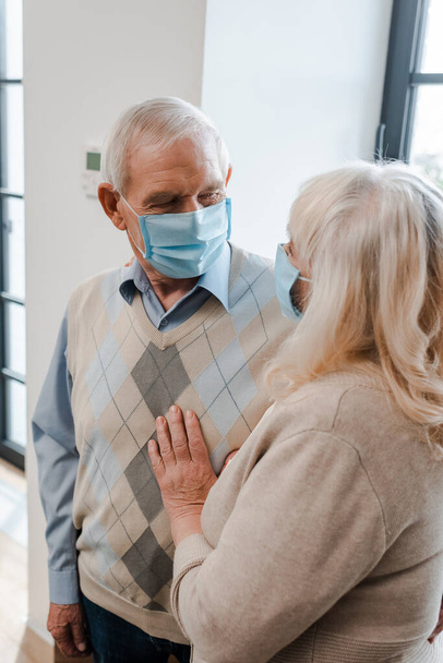 sad senior couple in medical masks hugging at home during self isolation - Foto, immagini