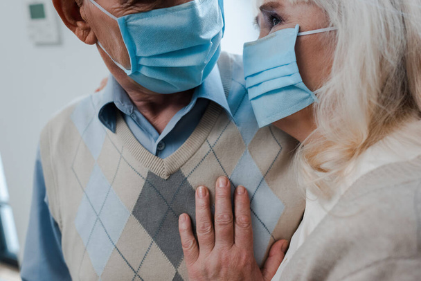 cropped view of elderly couple in medical masks hugging at home during self isolation - Valokuva, kuva