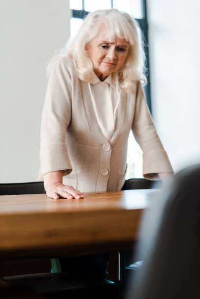 upset elderly woman standing at table during self isolation, selective focus - Foto, Imagem