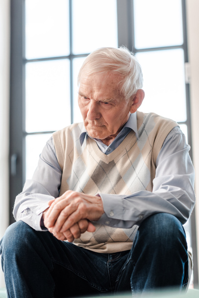 upset senior man sitting alone on sofa during self isolation - Photo, image