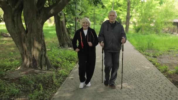 アクティブシニア老夫婦。ノルディックウォーキングの訓練公園を走る女性 - 映像、動画